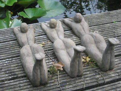 three stone sculptures sitting on top of a wooden surface next to water and plants in the background