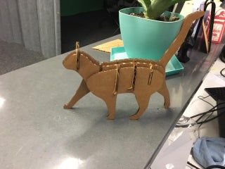 a small wooden cat sitting on top of a counter next to a potted plant