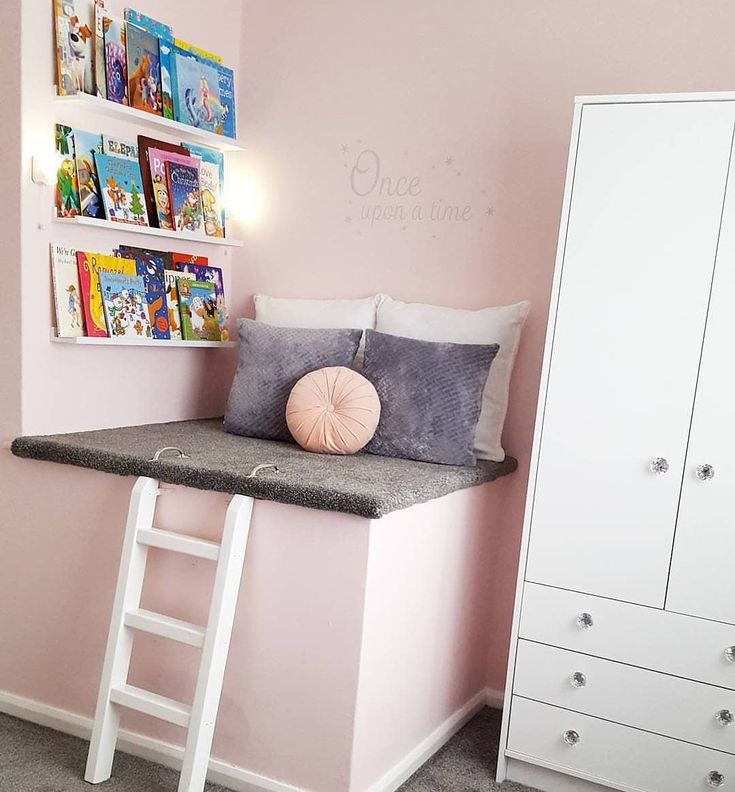 a bedroom with pink walls and grey carpeted flooring, white furniture and shelves on the wall