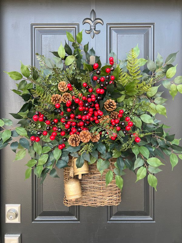 a basket filled with holly, berries and pine cones hanging from a front door handle