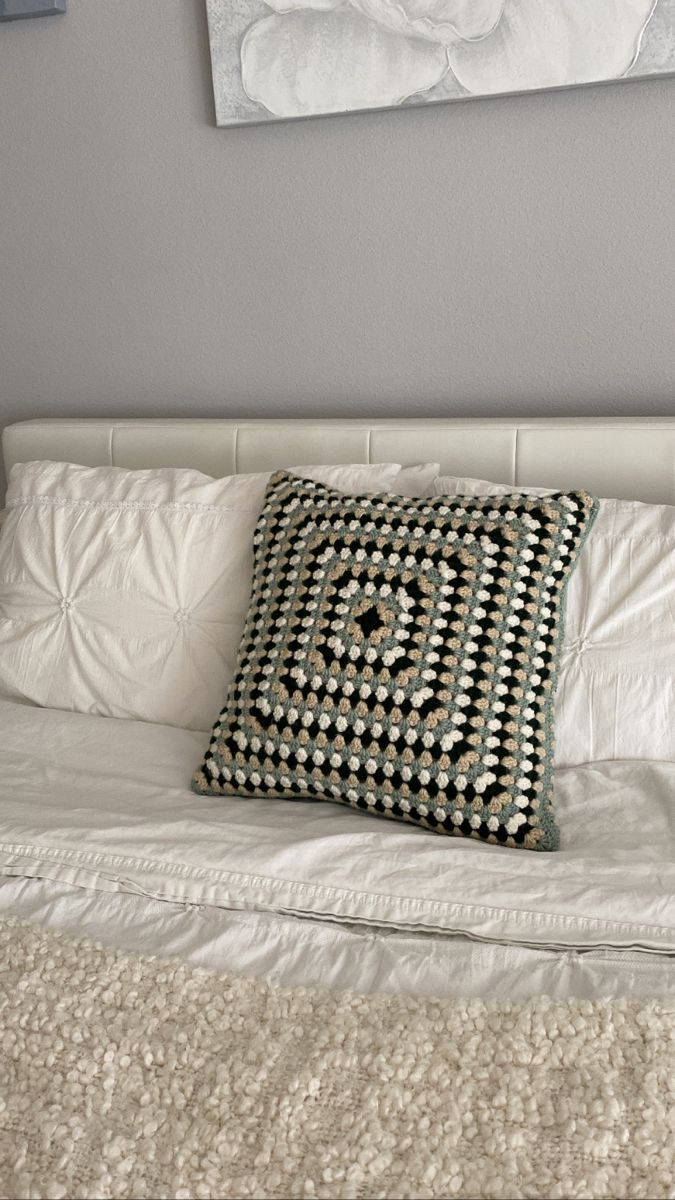 a bed with white sheets and a black and white square pillow on top of it