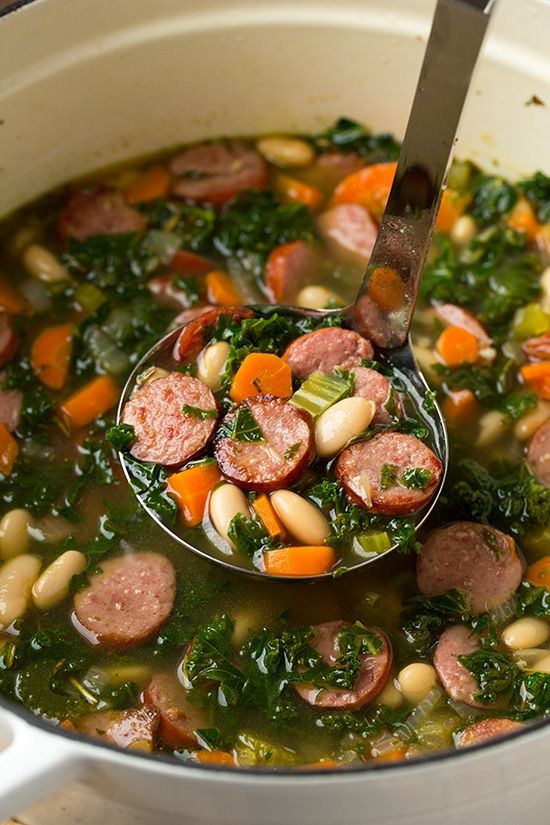 a ladle full of soup with sausage, beans and kale in the pot