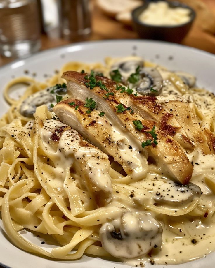 a white plate topped with pasta covered in sauce and chicken breast pieces on top of it