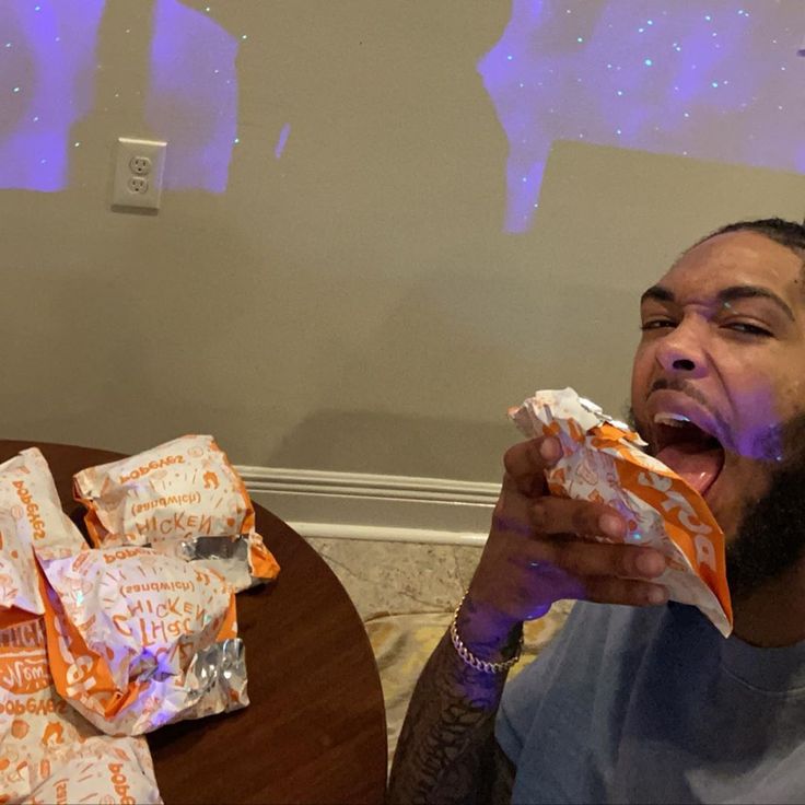 a man sitting at a table eating something with his mouth open and wrapped in foil