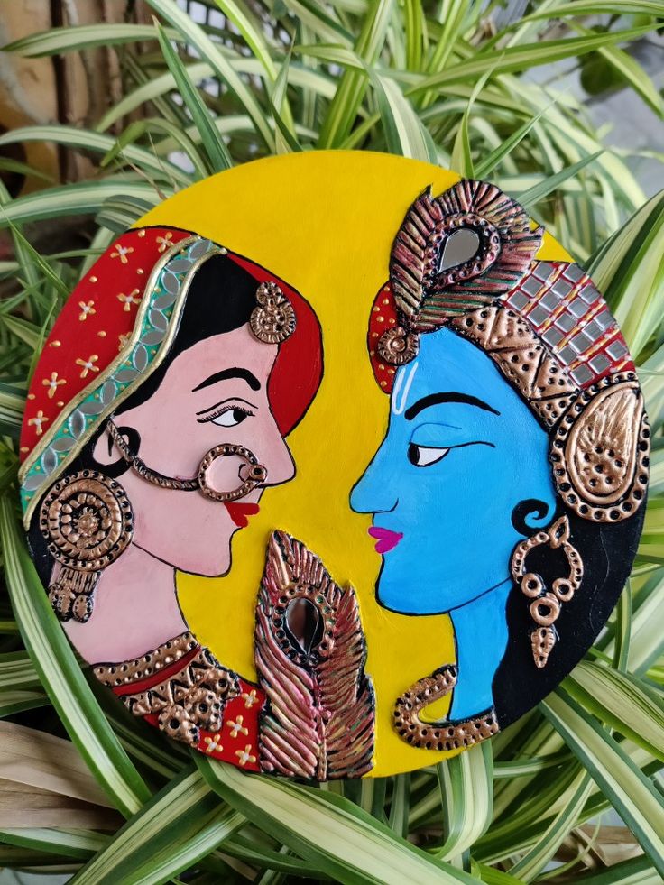 two painted faces on a yellow and blue disc next to plants with green leaves in the background