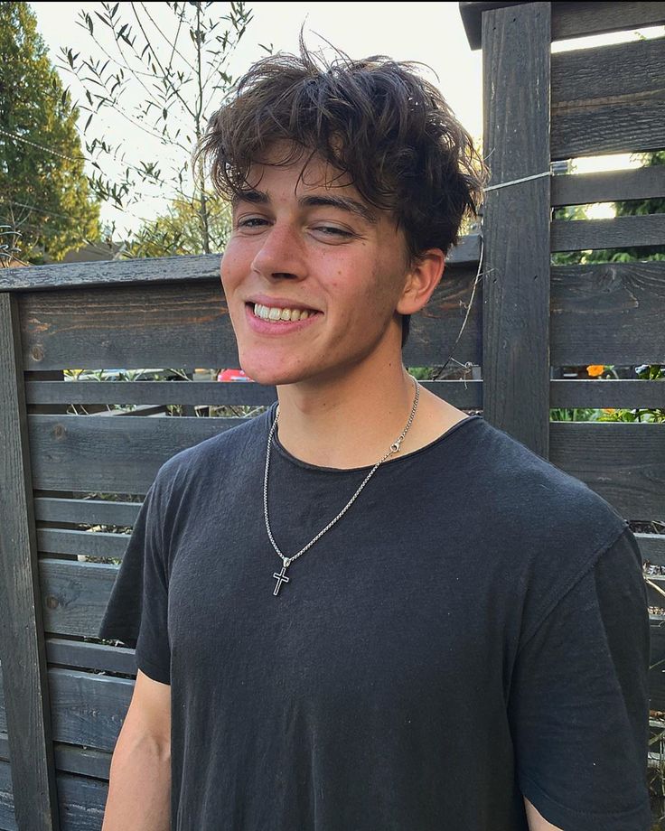 a young man standing in front of a wooden fence with a toothbrush in his mouth