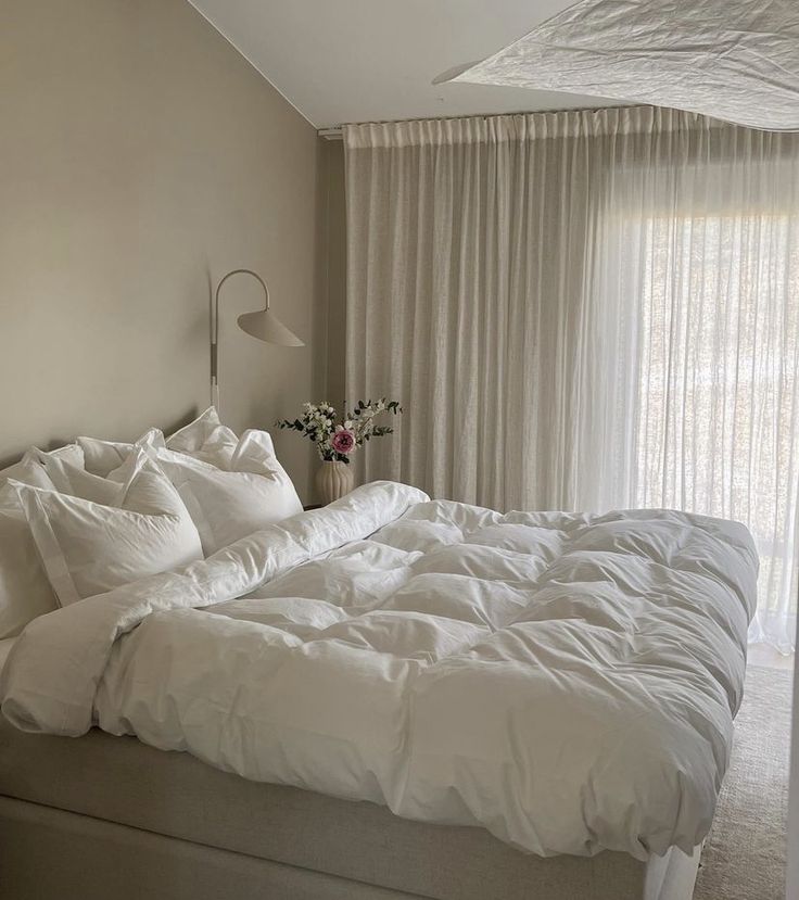 a large bed with white sheets and pillows in a bedroom next to a curtained window