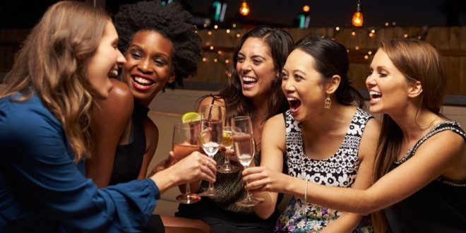 group of young women toasting with wine glasses in a restaurant or bar at night