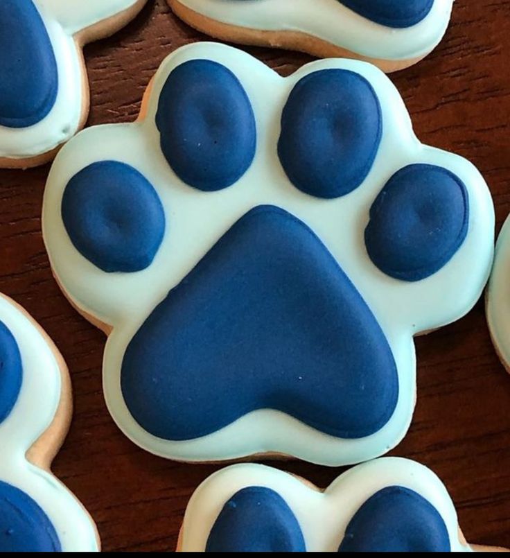 cookies with blue and white icing shaped like paw prints on top of a wooden table