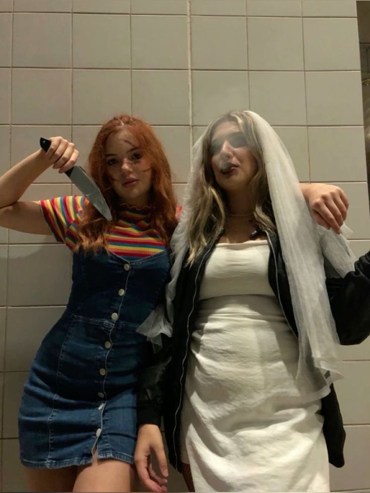 two women standing next to each other in front of a wall with white tiles on it