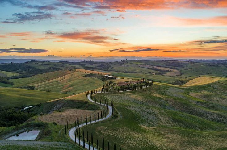 an aerial view of a winding road in the countryside at sunset or sunrise with colorful clouds