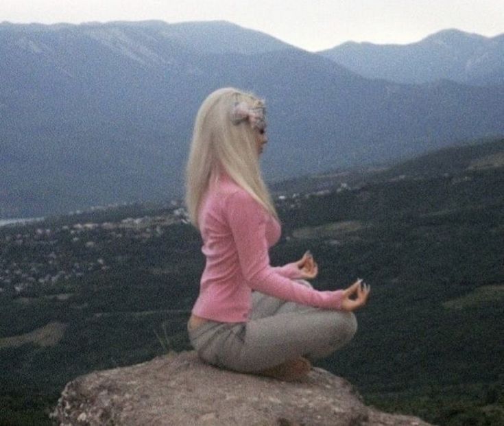 a woman sitting on top of a rock with her legs crossed and looking out at the mountains