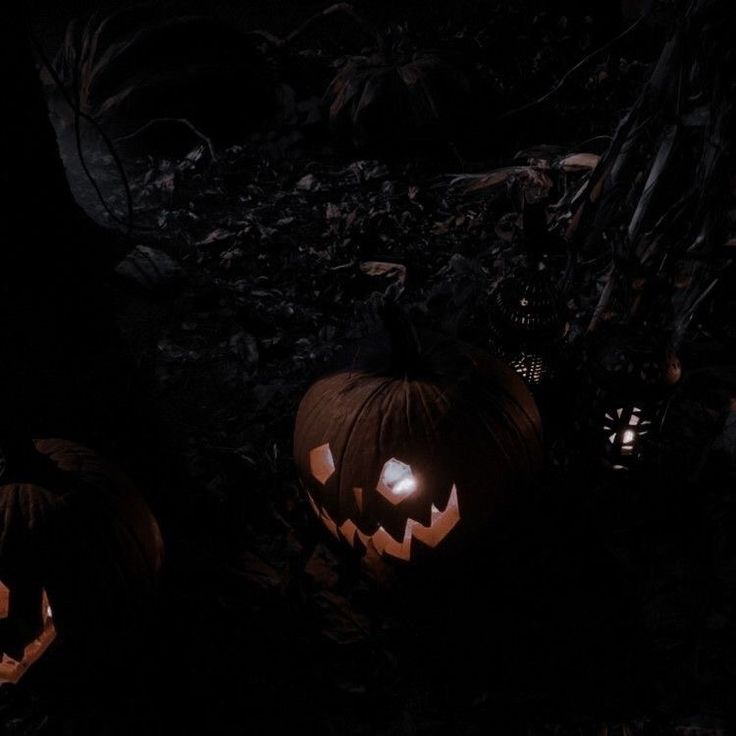 two carved pumpkins sitting in the dark with their faces lit up and one glowing