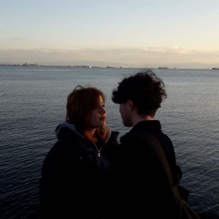 two people standing next to each other near the water