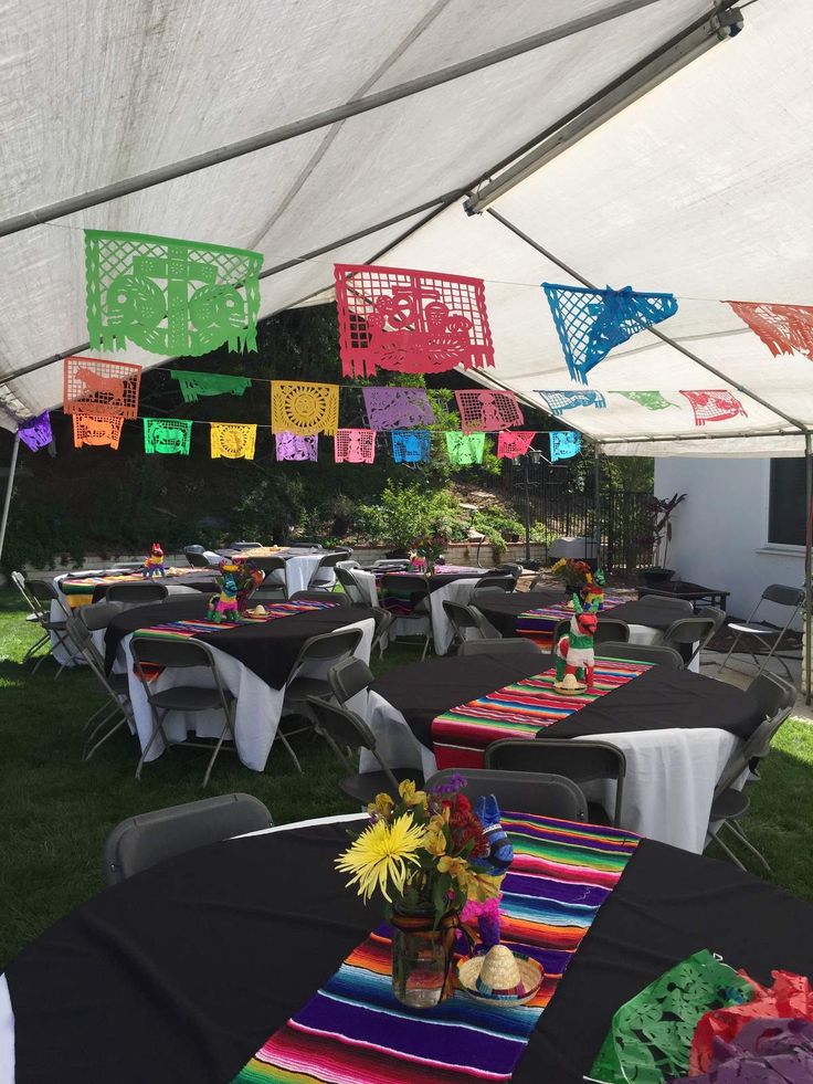 tables and chairs are set up under a tent for an outdoor party with colorful decorations