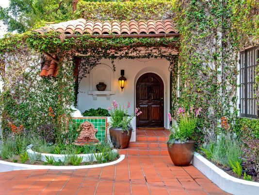 the front entrance to a house covered in vines and potted plants, with two large planters on either side