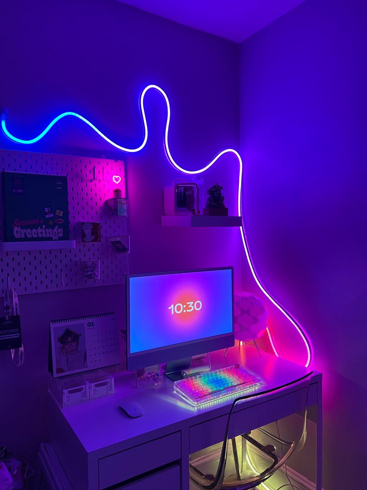 a desk with a computer and neon lights on the wall in a room that is lit up