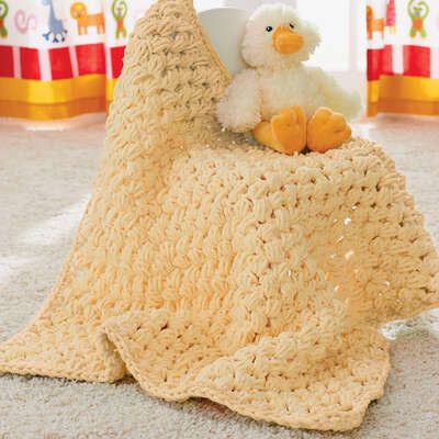 a crocheted blanket on the floor with a stuffed duck sitting on top of it