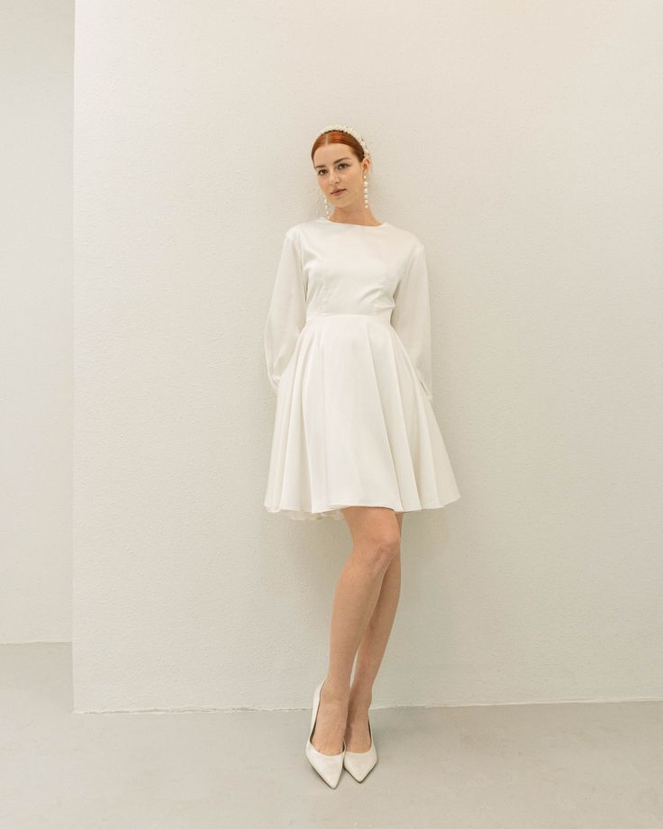 a woman standing in front of a wall wearing a white dress and high heel shoes