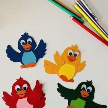 four different colored birds on a white surface next to pencils and crayons