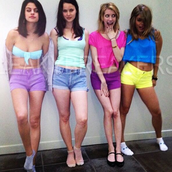 four girls standing in front of a wall with their hands on their hipss and wearing short shorts