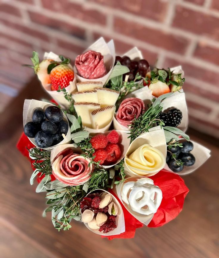 a bouquet of fruit, cheese and berries on a wooden table next to a brick wall