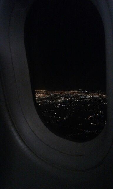 an airplane window looking out at the city lights in the dark night sky from inside