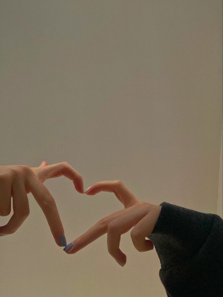 two hands making the shape of a heart with their fingers, against a white wall