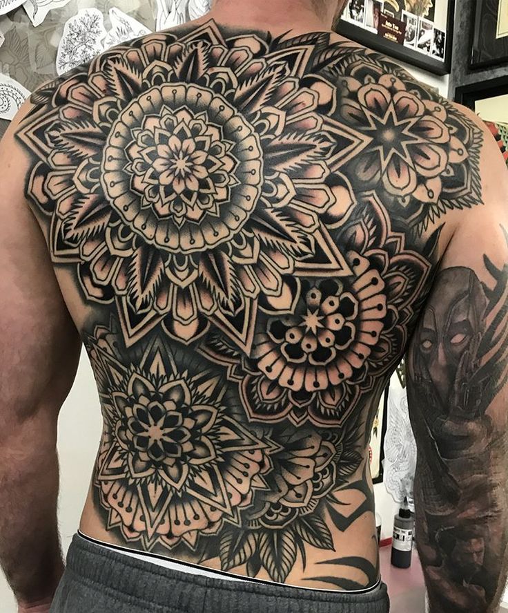 the back of a man's body with an intricate tattoo design on his chest