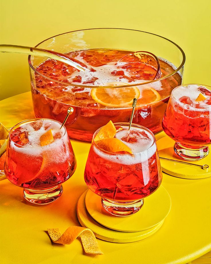 three glasses filled with drinks sitting on top of a yellow table next to orange slices