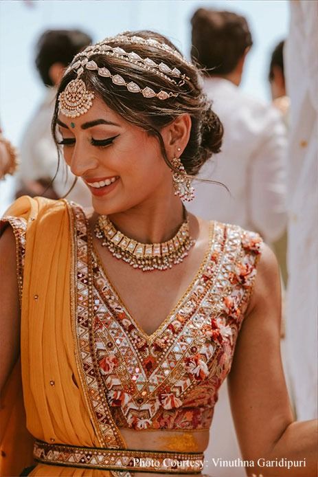 a woman in an orange and gold sari smiles as she walks down the aisle