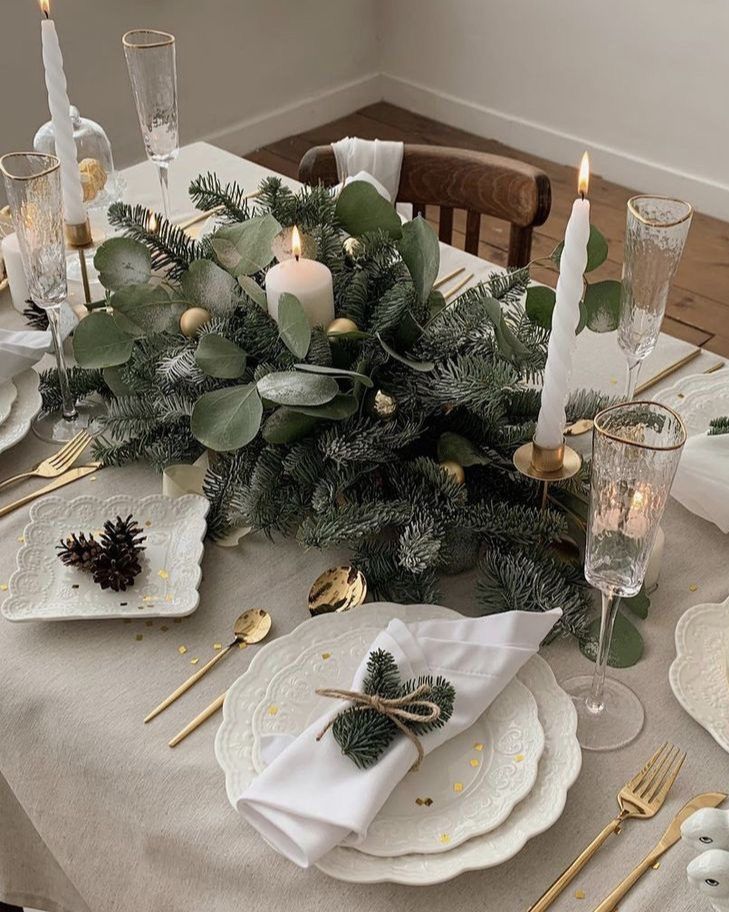 the table is set with white plates, silverware and greenery for christmas dinner