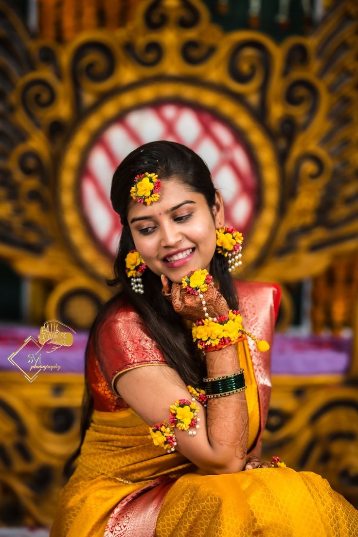 a woman in yellow and red sari sitting on a chair with flowers around her neck