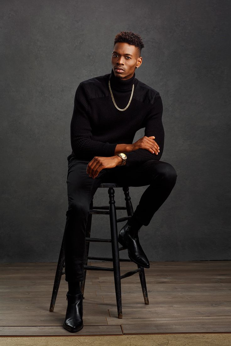 a man sitting on top of a wooden stool wearing a black sweater and pearls necklace