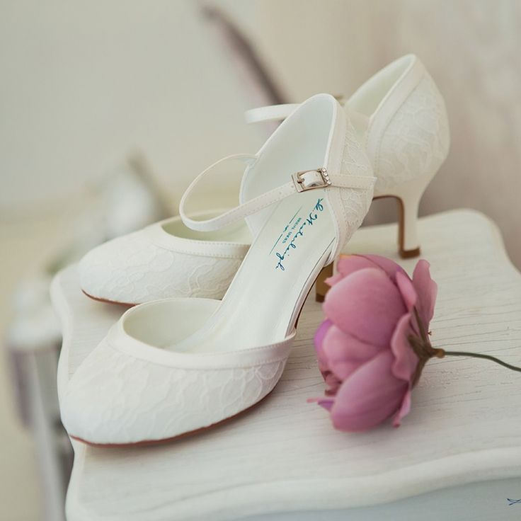 a pair of white shoes sitting on top of a table next to a pink flower