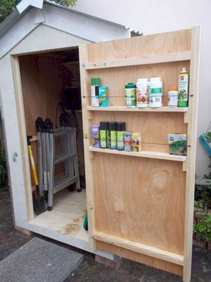 a storage shed with the door open and shelves full of various items in front of it