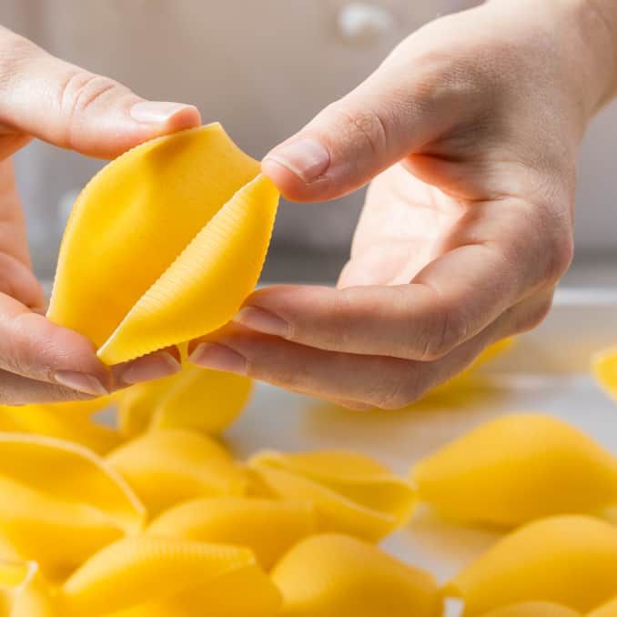 two hands are peeling yellow pasta on a white surface