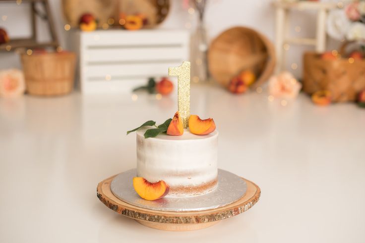 a white cake sitting on top of a table with peach slices around it and the number one frosted in gold