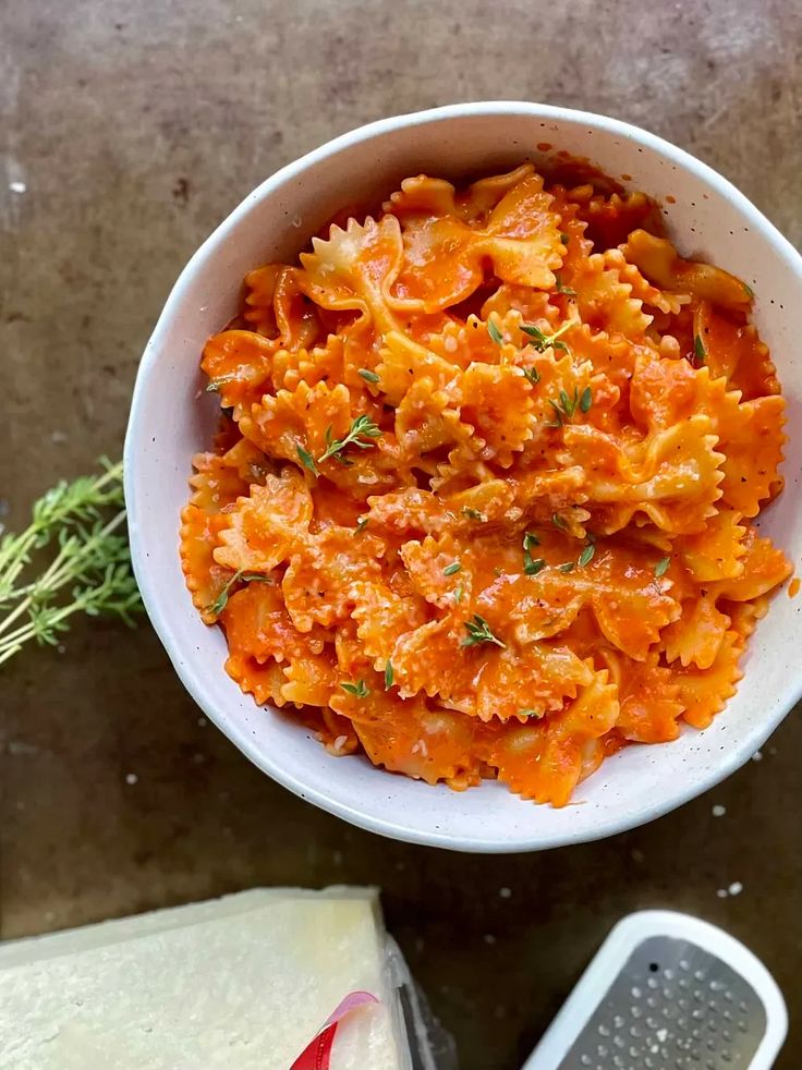 a white bowl filled with pasta next to a grater