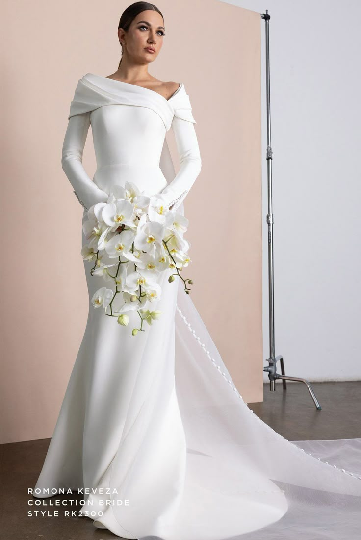 a woman in a white wedding dress with flowers on her shoulder and long sleeves, posing for the camera