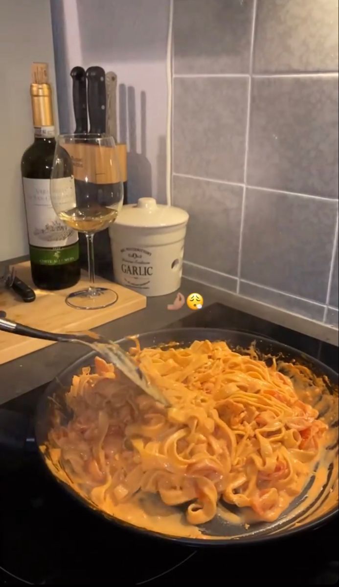 a pan filled with pasta next to a bottle of wine