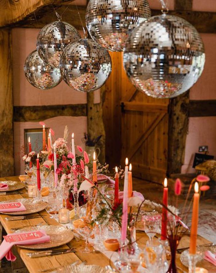 a long table is set with candles, plates and napkins as well as disco balls hanging from the ceiling