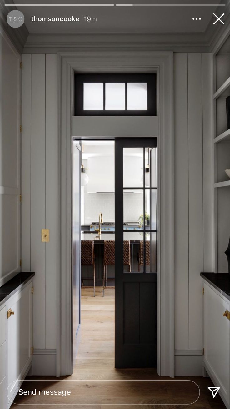 an open door leading to a kitchen with white walls and wood floors, along with black counter tops