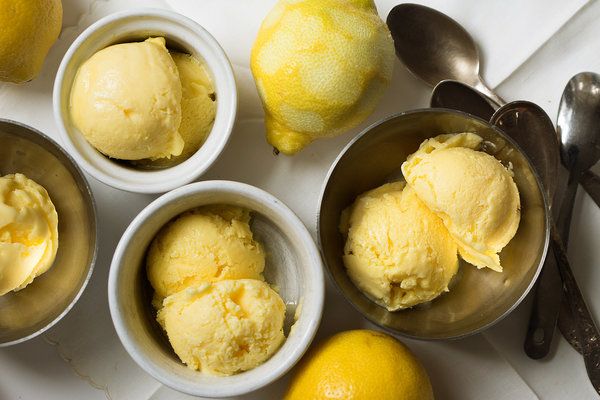 four bowls filled with ice cream next to lemons and spoons on a table