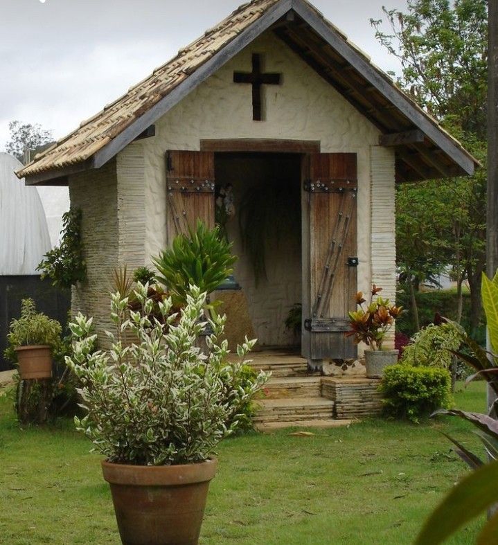 a potted plant sits in front of a small house with a cross on the door