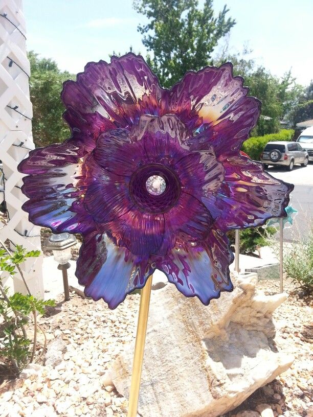 a large purple flower sitting on top of a wooden stick in front of a building