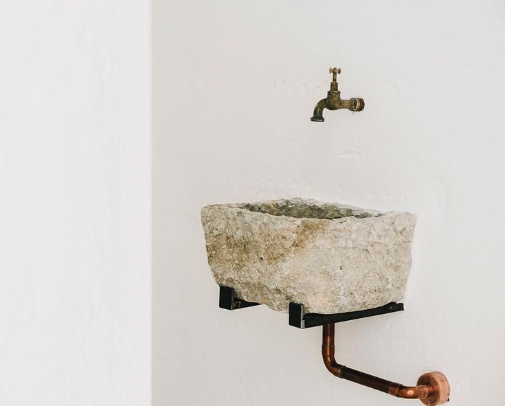 a stone sink mounted to the side of a wall next to a faucet