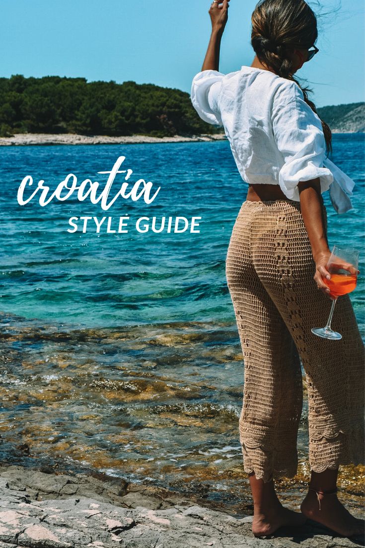 a woman standing on top of a rocky beach next to the ocean holding a drink