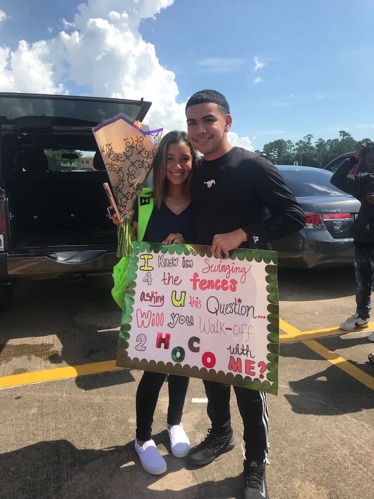 a man and woman standing next to each other in front of a car holding a sign