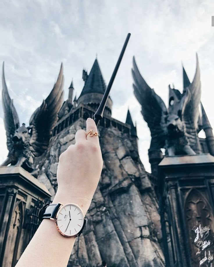 a hand holding a wand in front of a castle